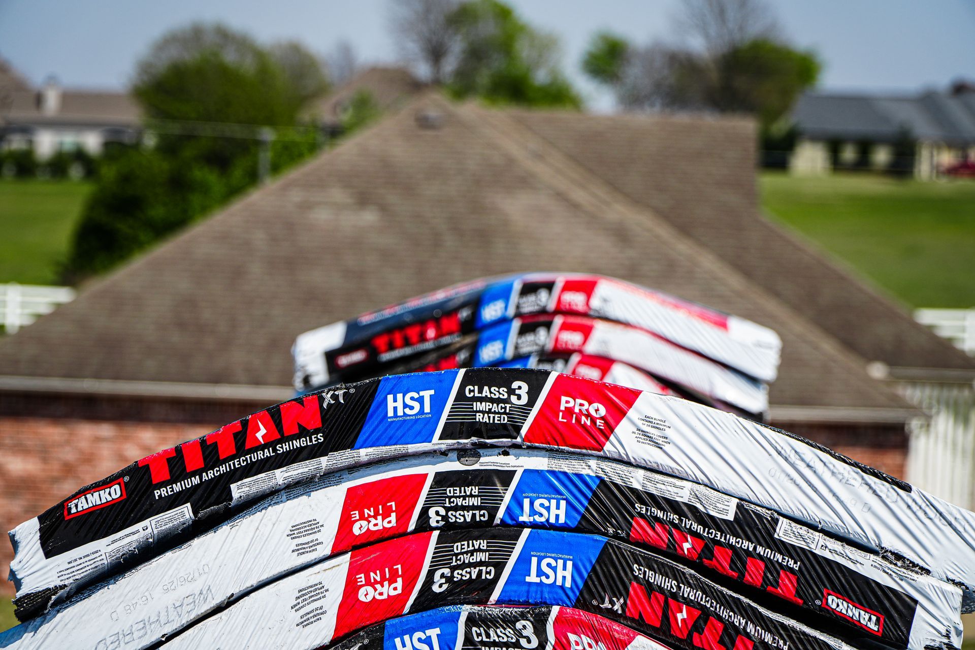 Stacked roofing shingles on a house roof with a suburban neighborhood in the background