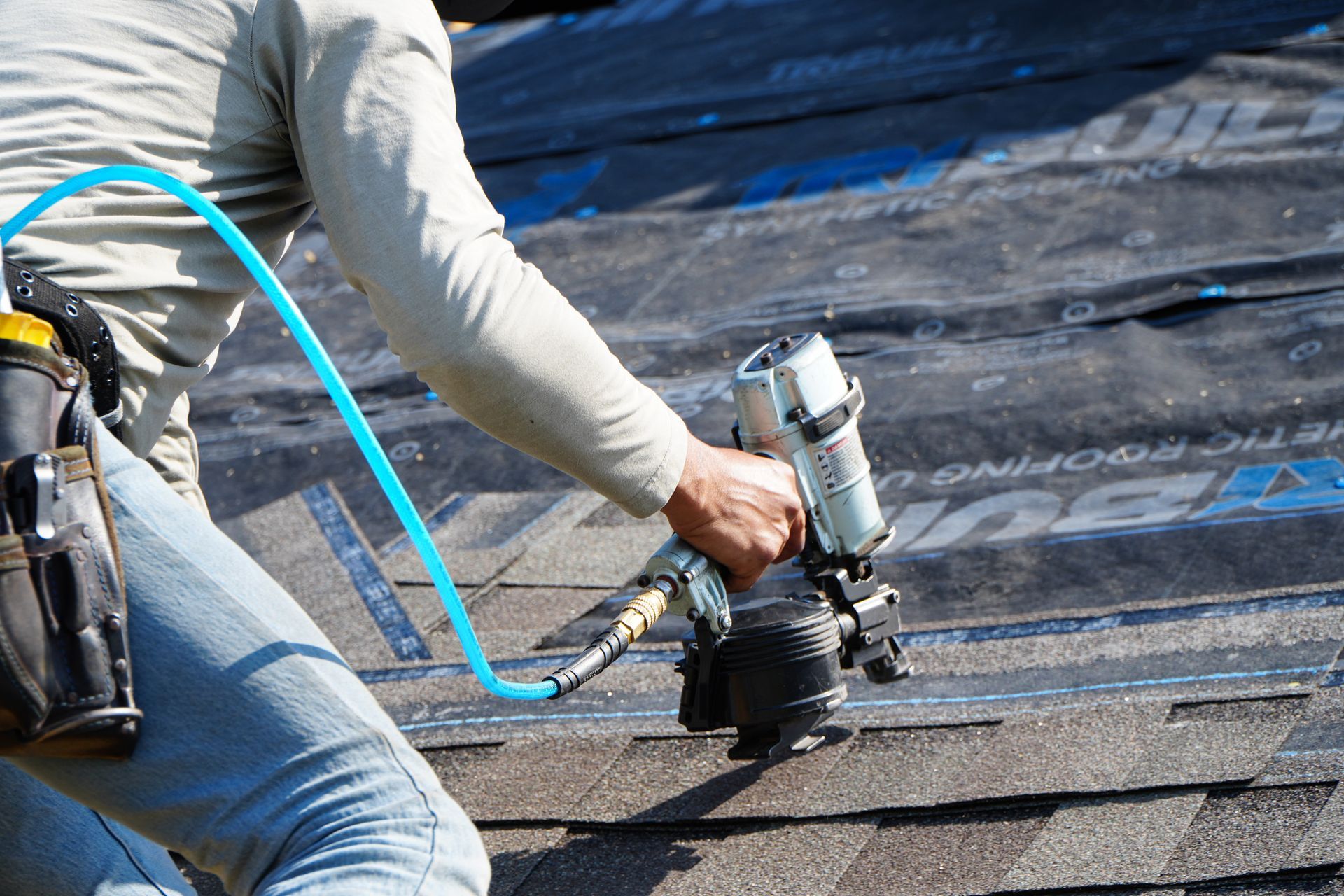 Worker using a nail gun to install shingles on a roof
