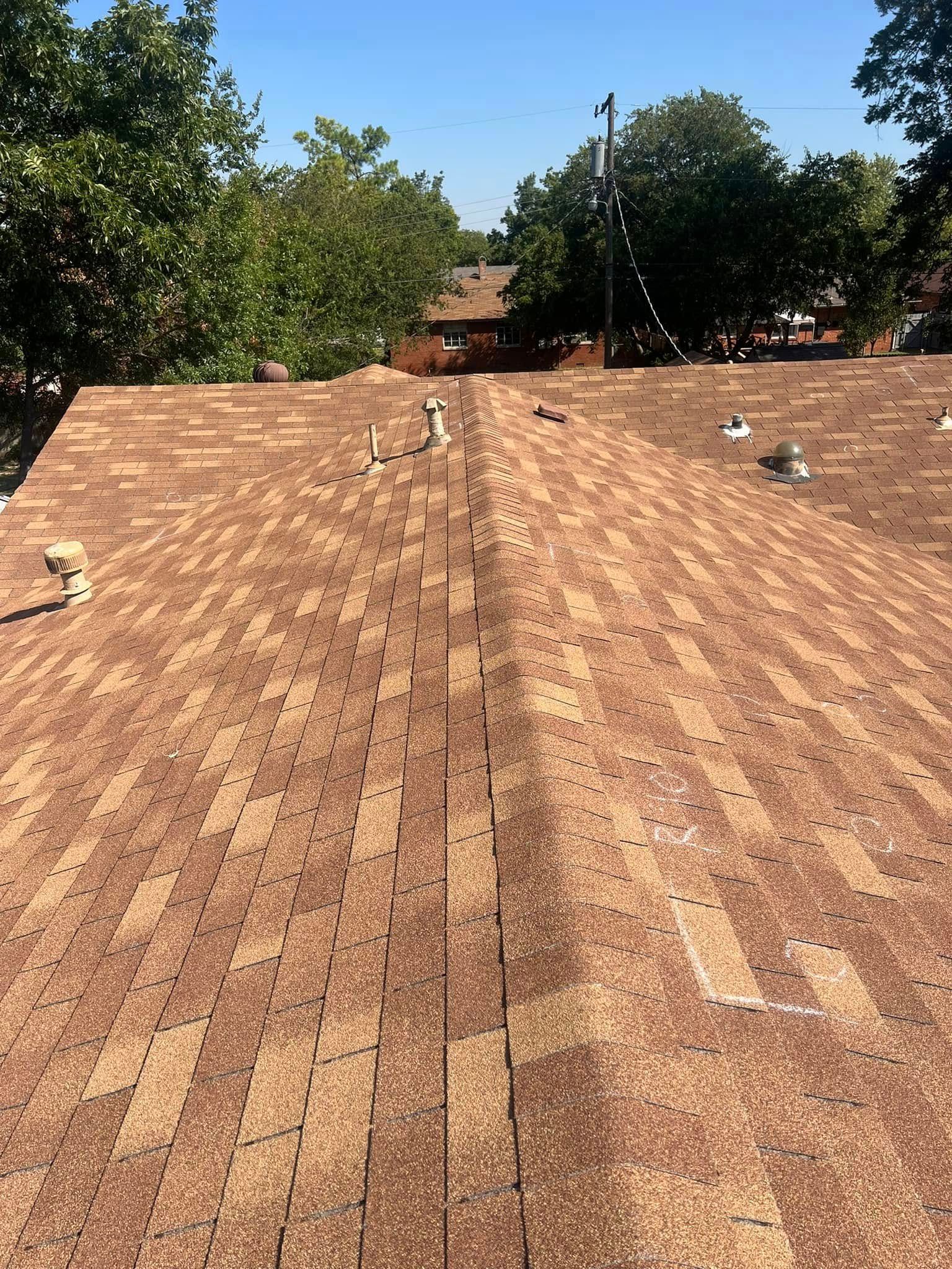 Rooftop with reddish shingles and several roof vents, bordered by green trees under a clear sky