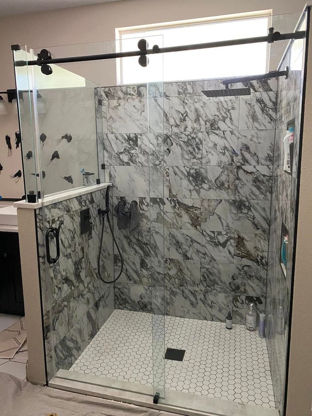 Glass shower stall with marble-pattern walls and white tiled floor in a bathroom