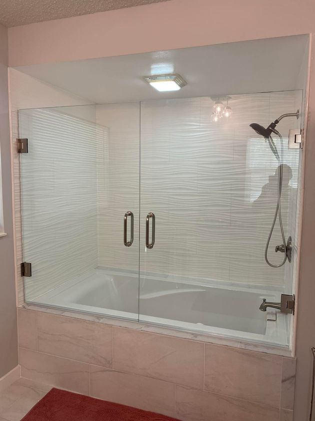 Glass shower enclosure with sliding doors, white tile walls, and a showerhead inside.