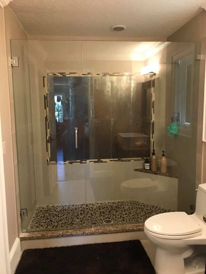 Bathroom with glass-enclosed shower, gray tile floor, beige walls, and a toilet in the foreground.