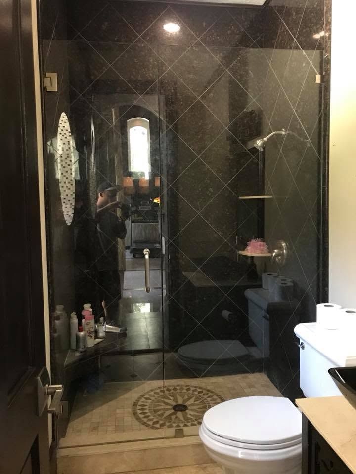 Modern bathroom with dark tiled walls, glass shower door, and white toilet in the foreground.
