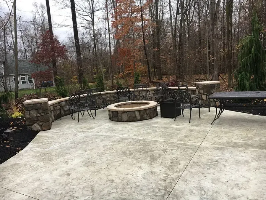 Patio with stone fire pit, curved seating wall, and outdoor furniture beside a wooded backyard.