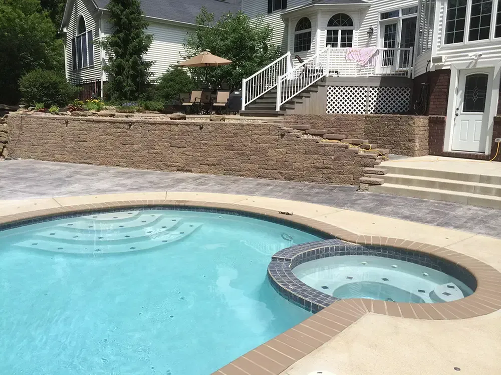 Backyard pool with a raised hot tub, stone retaining wall, and white house steps.