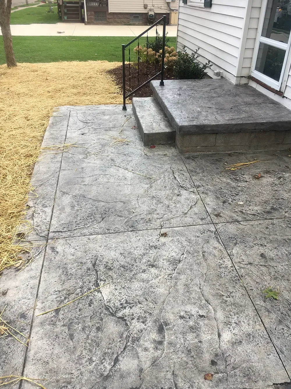 Cracked concrete walkway beside a house with a small step and yellowing grass.