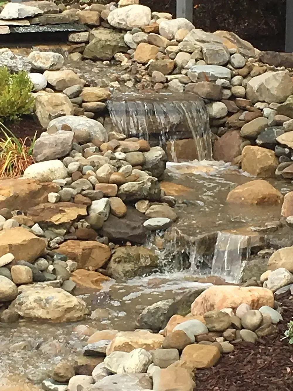 Rock garden waterfall with water cascading over stacked stones into a small stream
