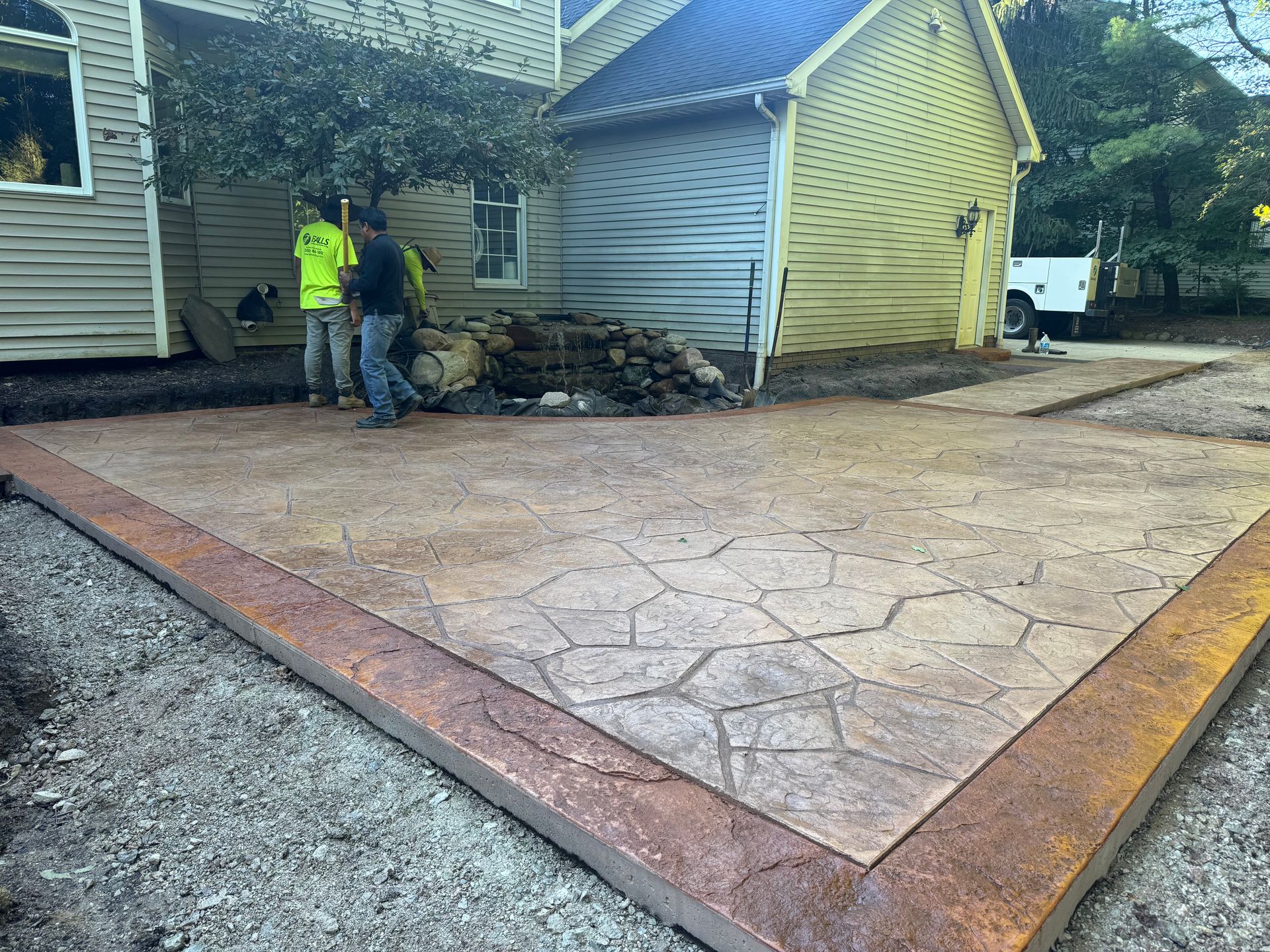 Workers repairing a cracked driveway beside a house with yellow siding and a blue roof