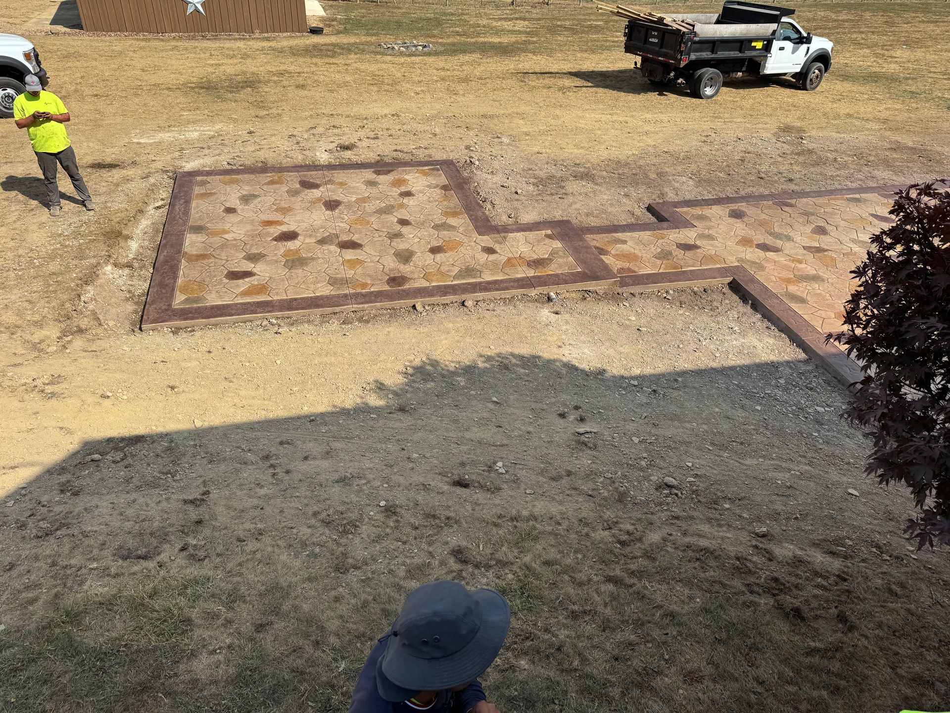 Workers and a utility truck near a large rectangular patch in a dry yard.