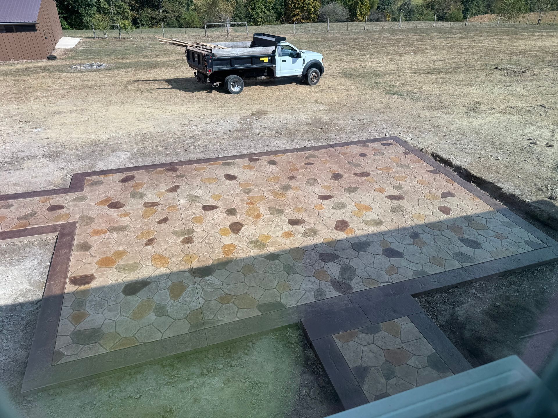 Pickup truck parked on a grassy lot beside a stone patio and steps, with a wooded background