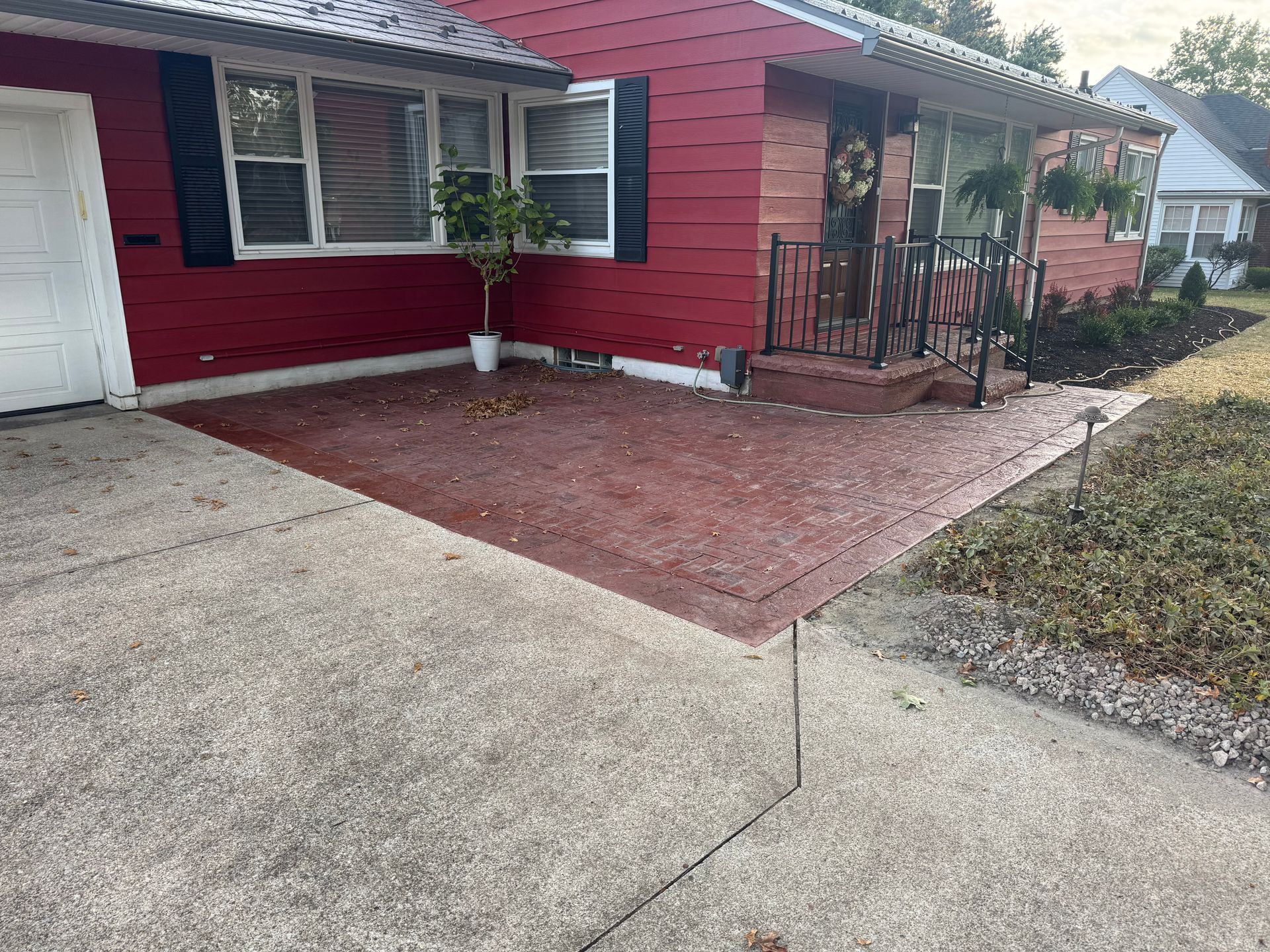 Red house exterior with driveway, front window, and small brick patio with railing.