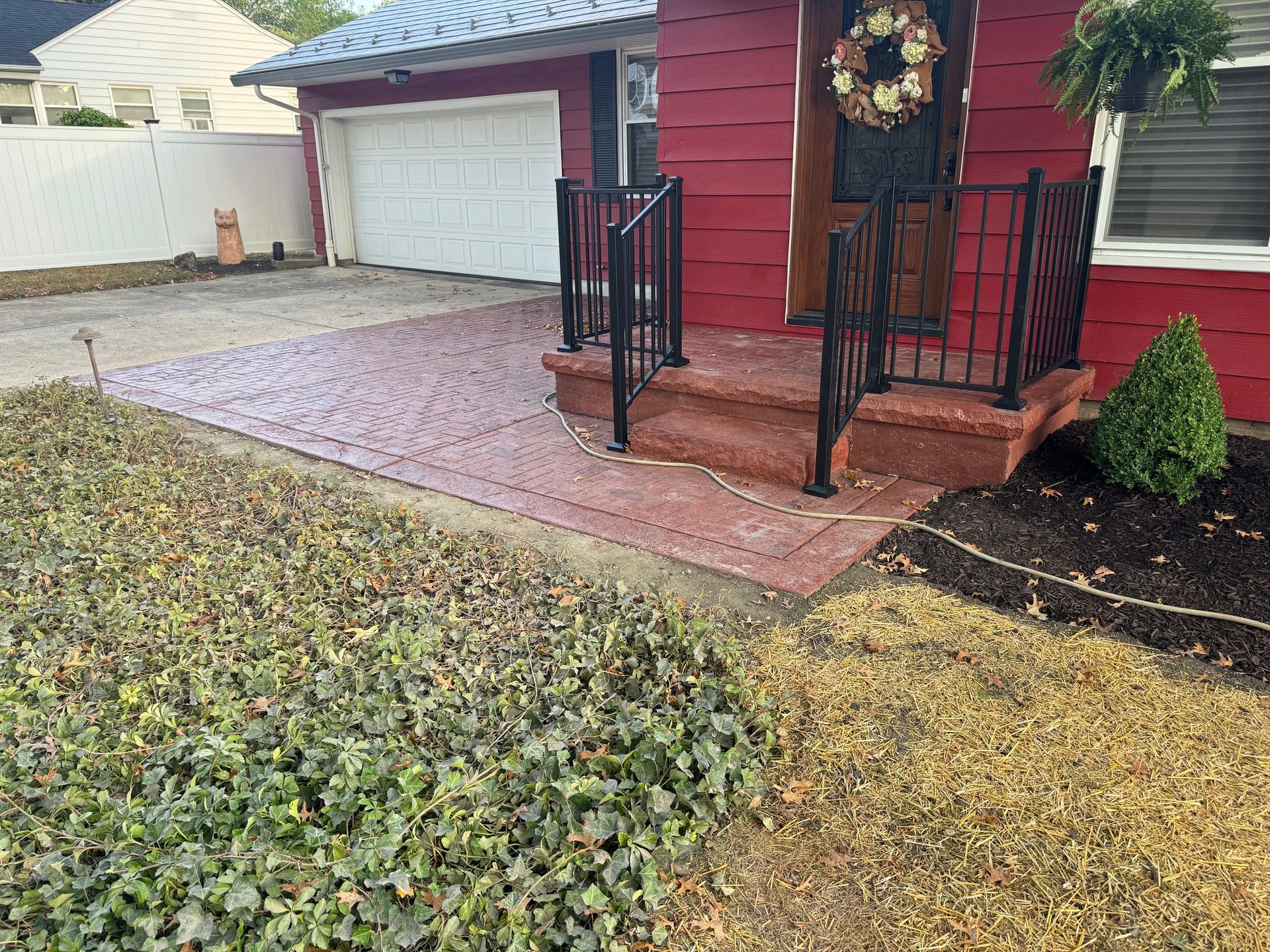 Red house porch with black railing, white garage, and a brick walkway bordered by winter groundcover.