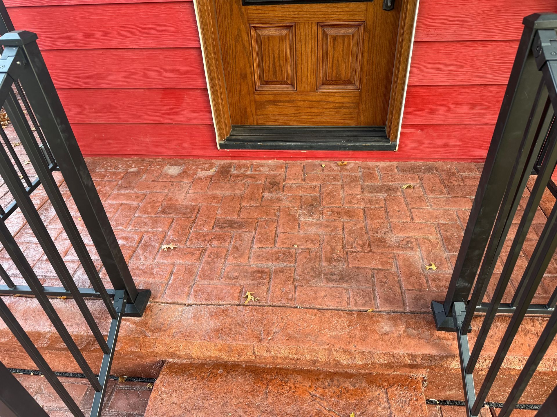 Brick front porch with red siding, wooden door, and black railings leading to a stoop