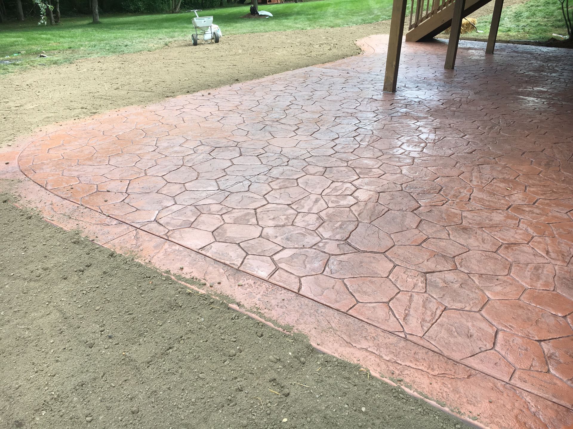 Cracked reddish patio beside a grassy yard, with a table leg at right and a small white garden ornament in back.