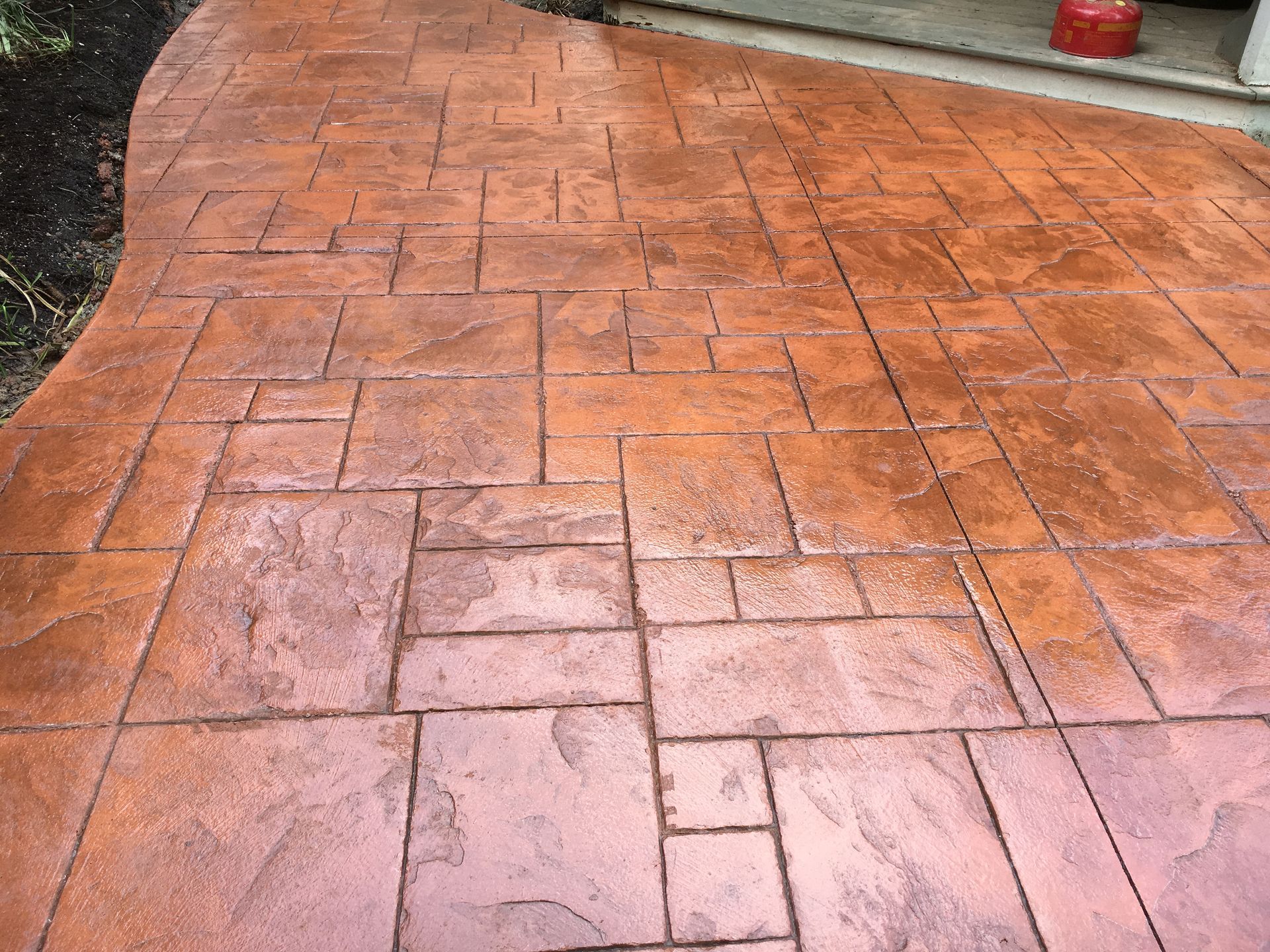 Wet terracotta-colored stamped concrete patio or walkway with a curved edge and tiled pattern