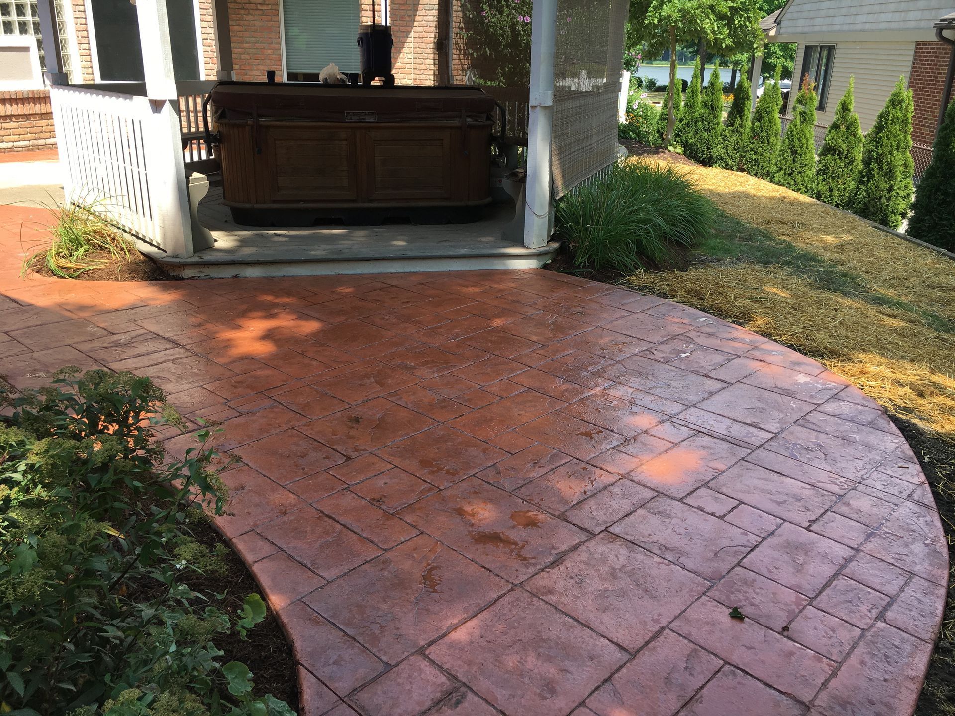 Curved red brick patio leading to a covered porch with a wooden bench and landscaped garden borders