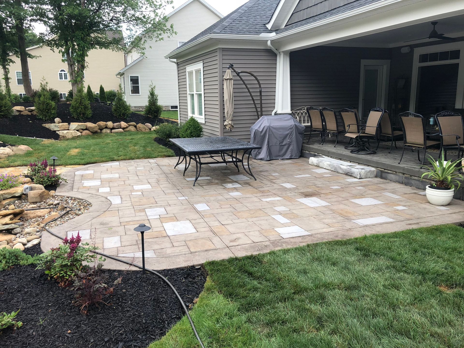 Patio with stone pavers, outdoor seating, grill, and garden landscaping beside a house