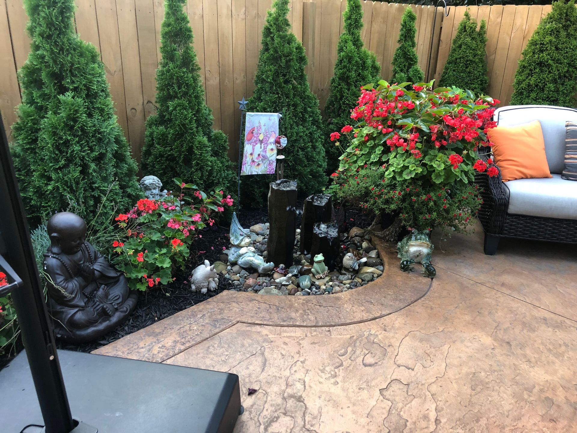 Backyard garden nook with potted flowers, small evergreens, a Buddha statue, and a cushioned chair