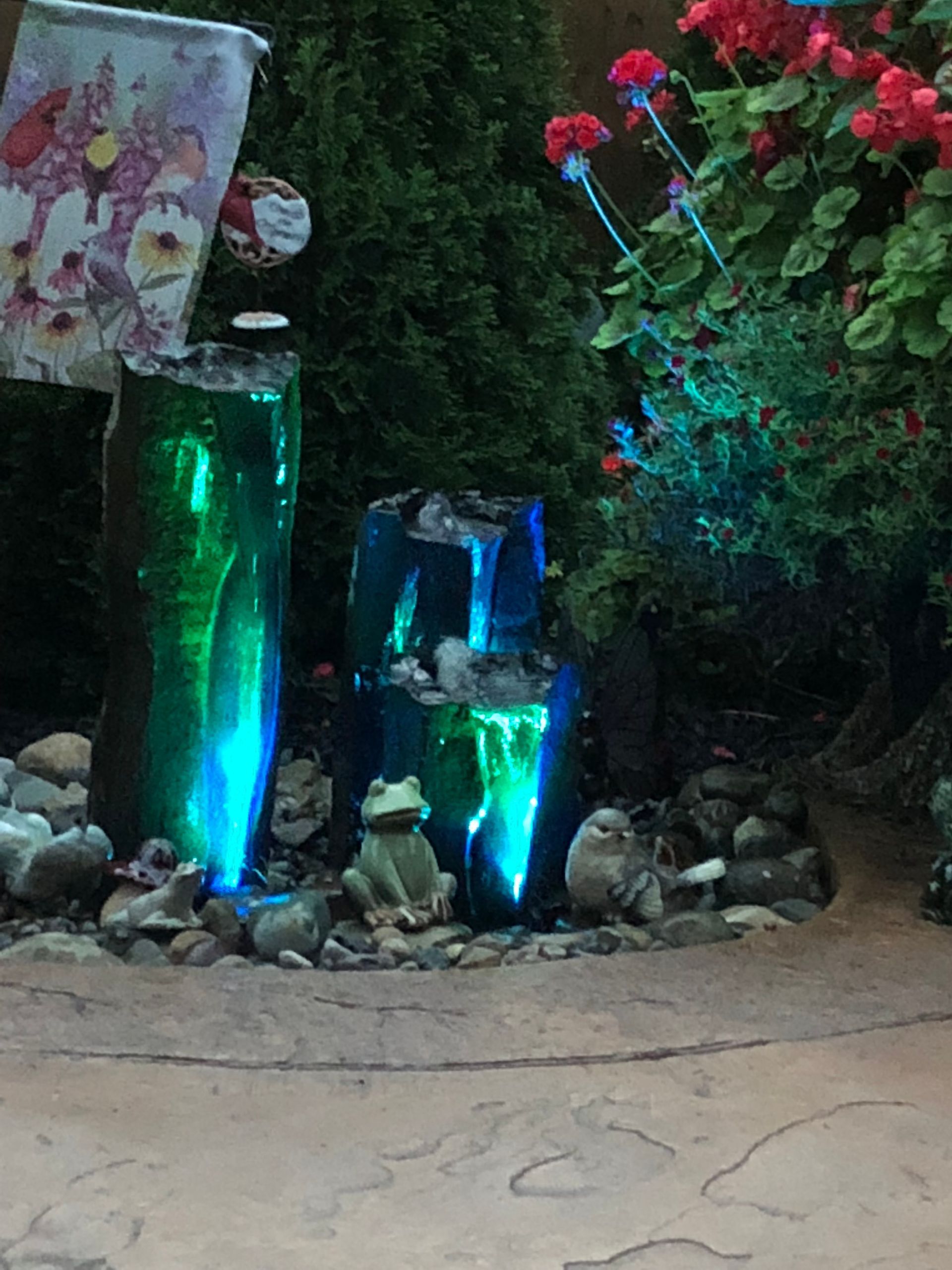 Night garden display with glowing blue-green glass bottles, rocks, and red flowers along a pathway