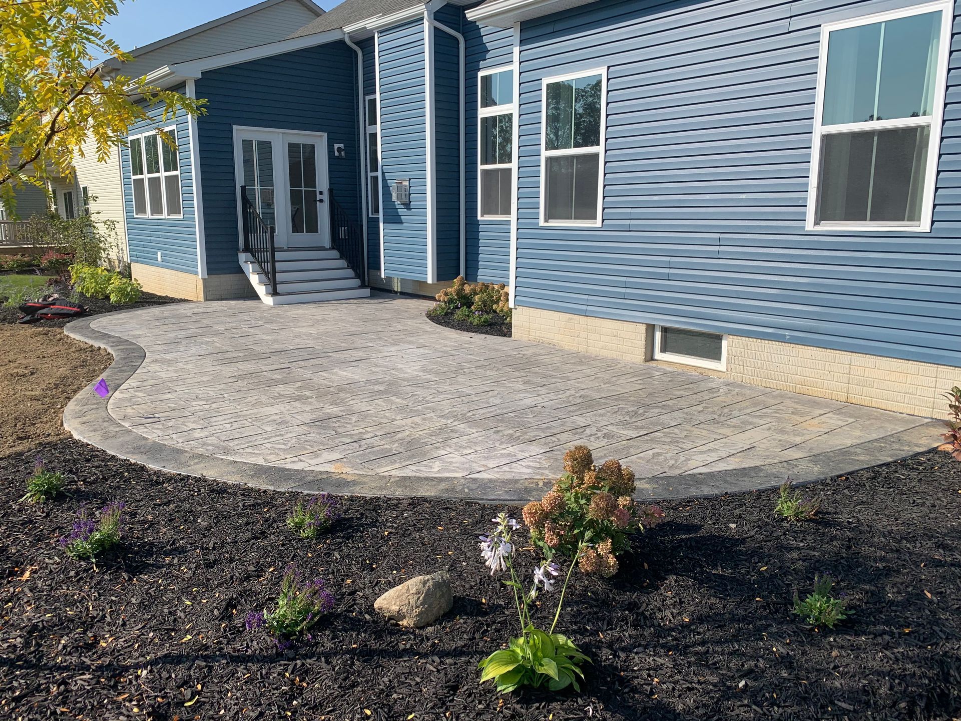 Blue house exterior with a concrete patio and dark mulch landscaping in front