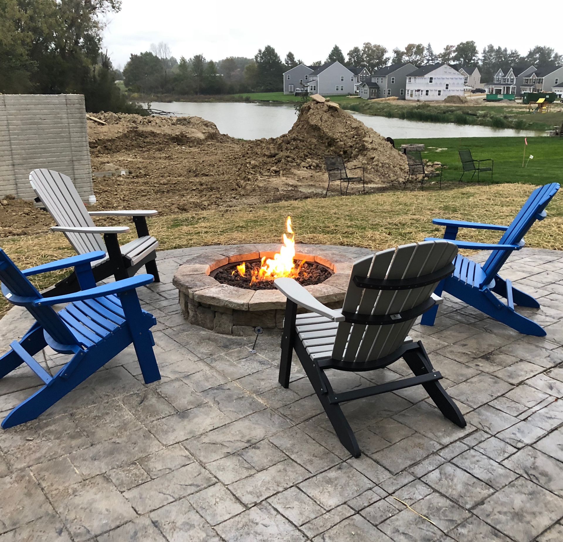 Backyard fire pit surrounded by four Adirondack chairs beside a pond at dusk