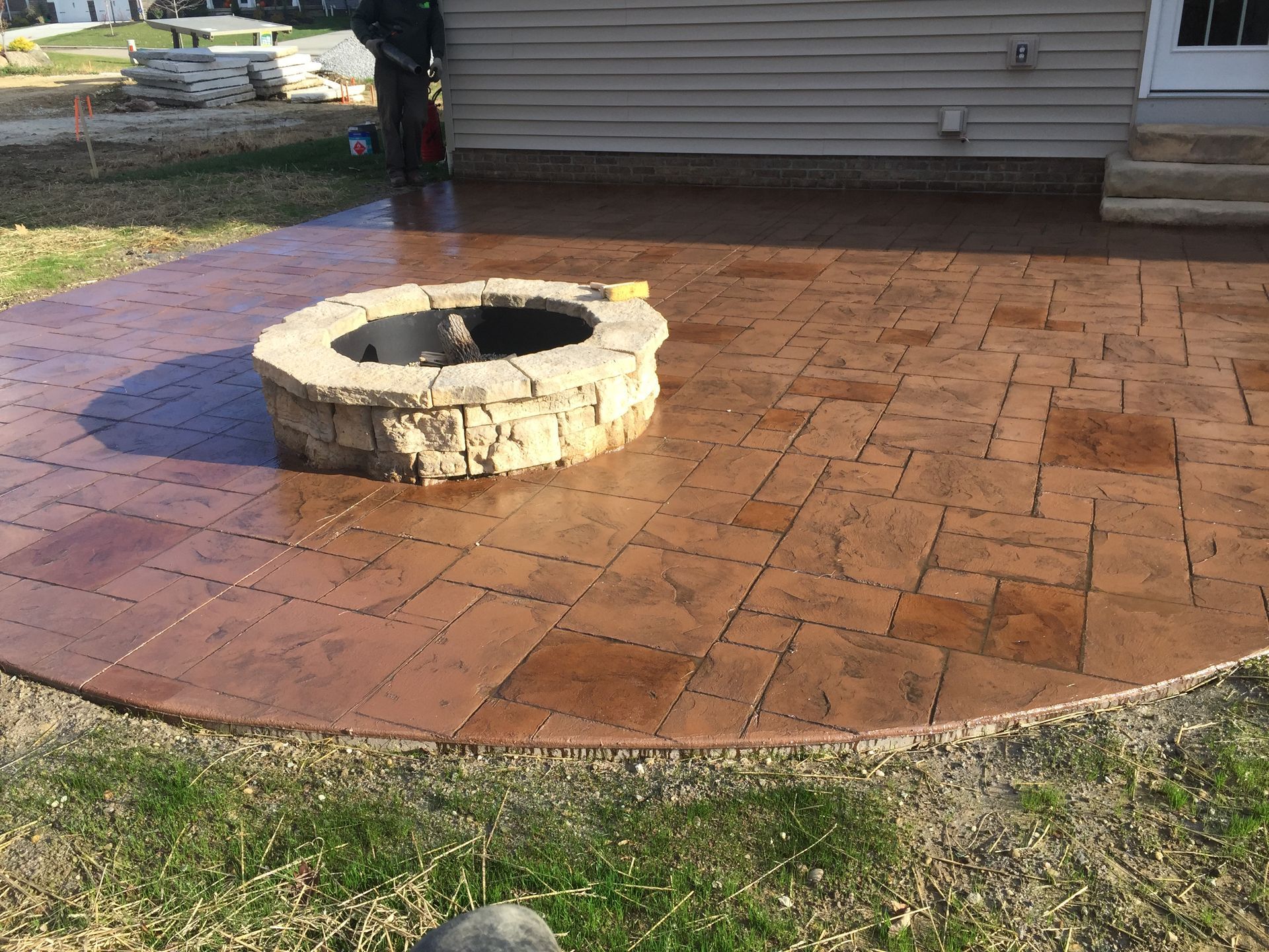 Brick patio with a stone fire pit beside a house and lawn
