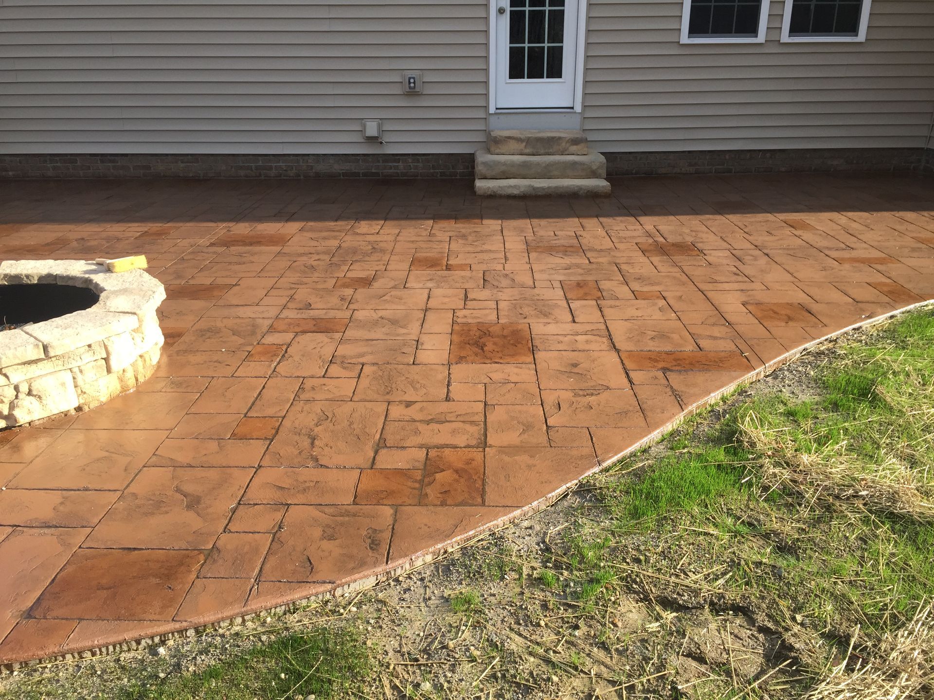 Stone patio and lawn beside a house, with a small stone fire pit on the left.