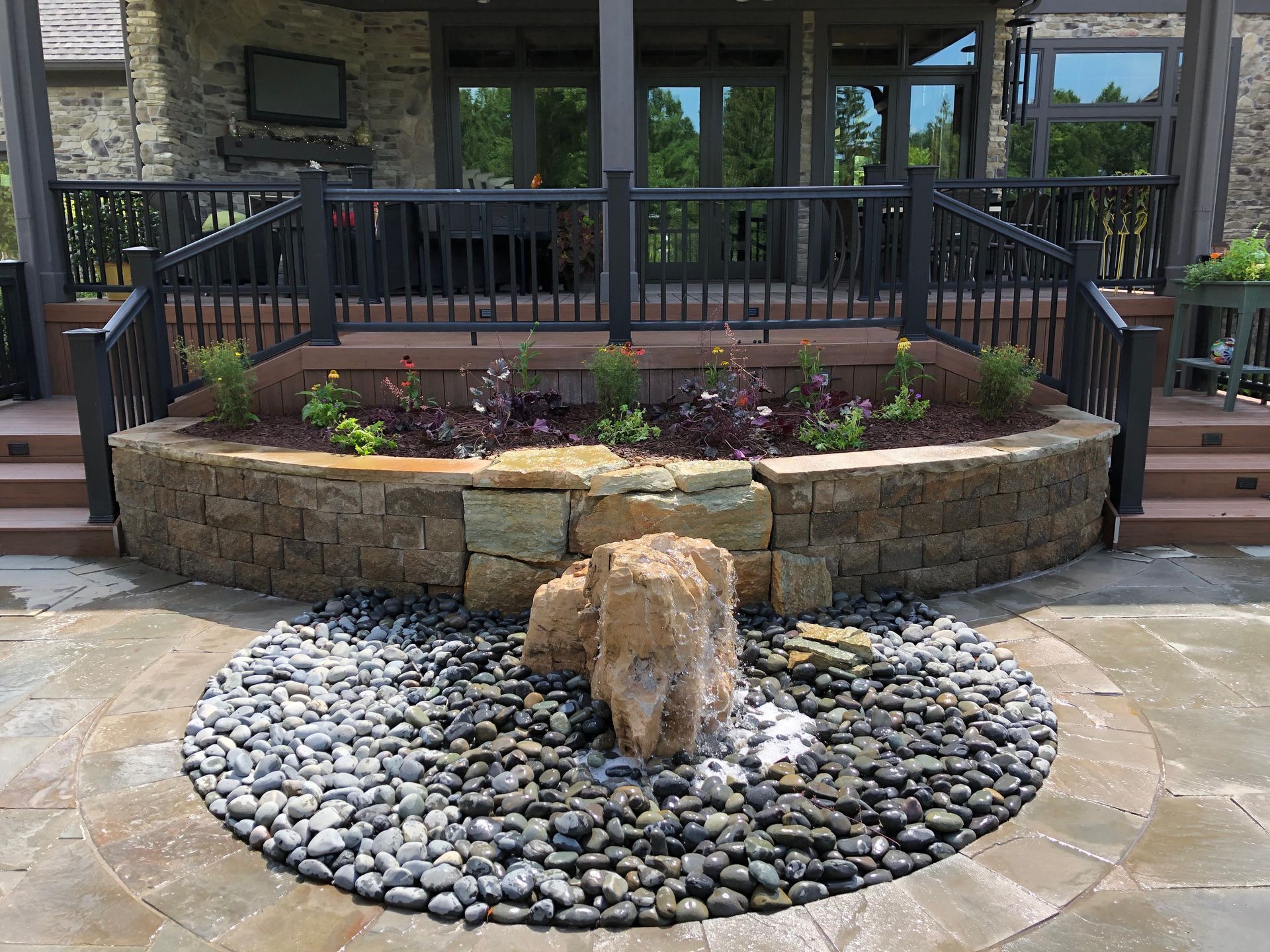 Rock garden with a central stone fountain in front of a porch and railing, surrounded by landscaping stones
