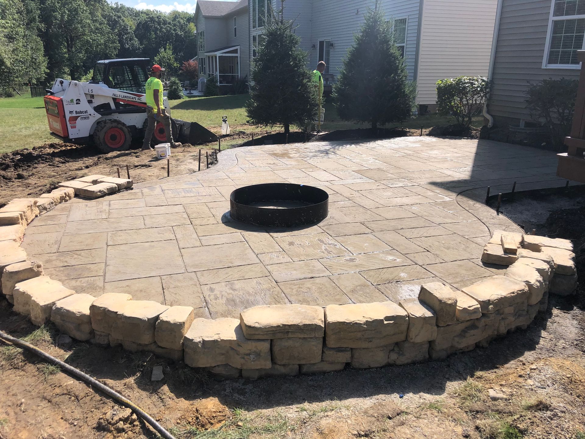 Partially built circular stone patio with fire pit in a suburban backyard, construction equipment nearby