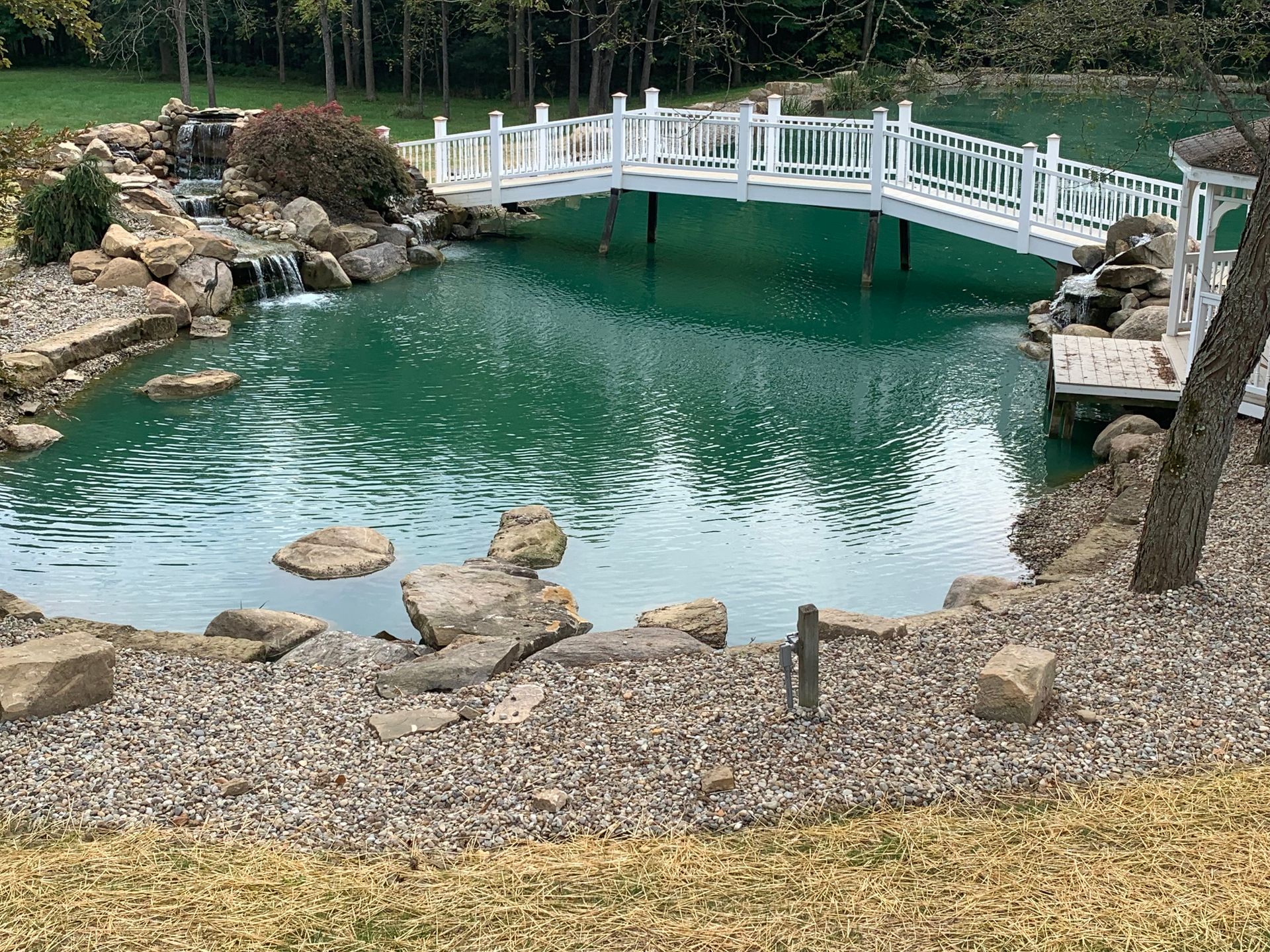 Small turquoise pond with rocks and a white footbridge in a landscaped garden