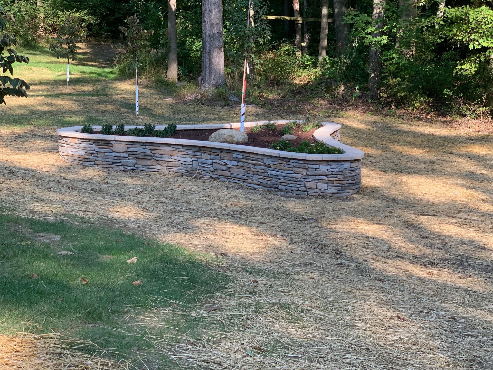 Backyard stone pond with white fountain posts, surrounded by grass and trees.
