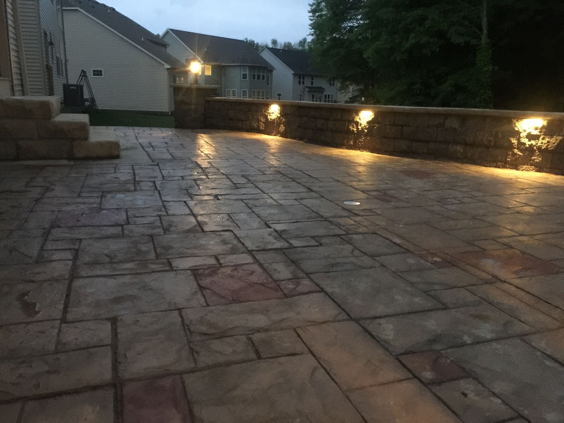 Stone patio at dusk with warm wall lights and houses in the background