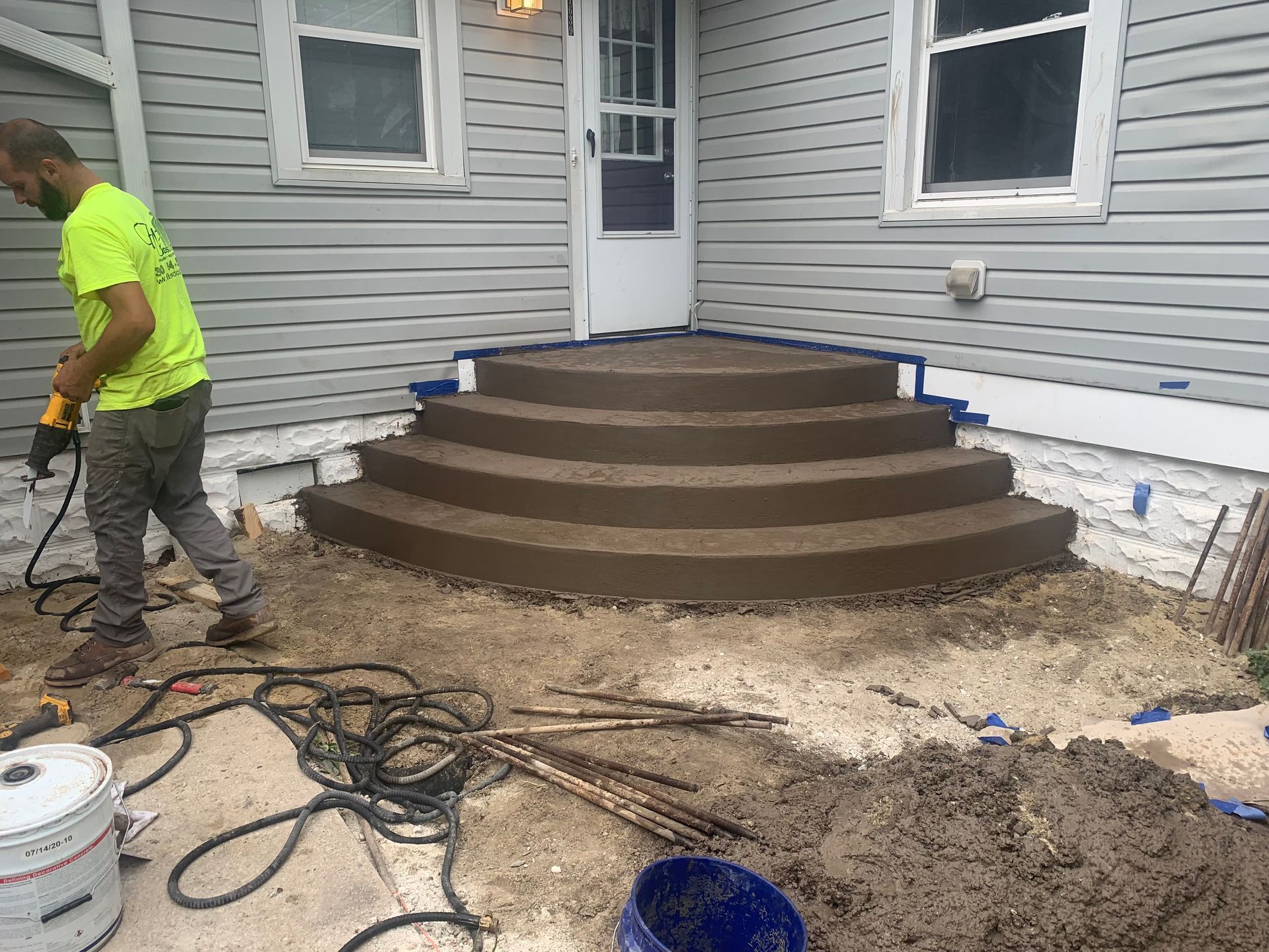 Worker building brown concrete steps in a gray house courtyard with tools and wet ground