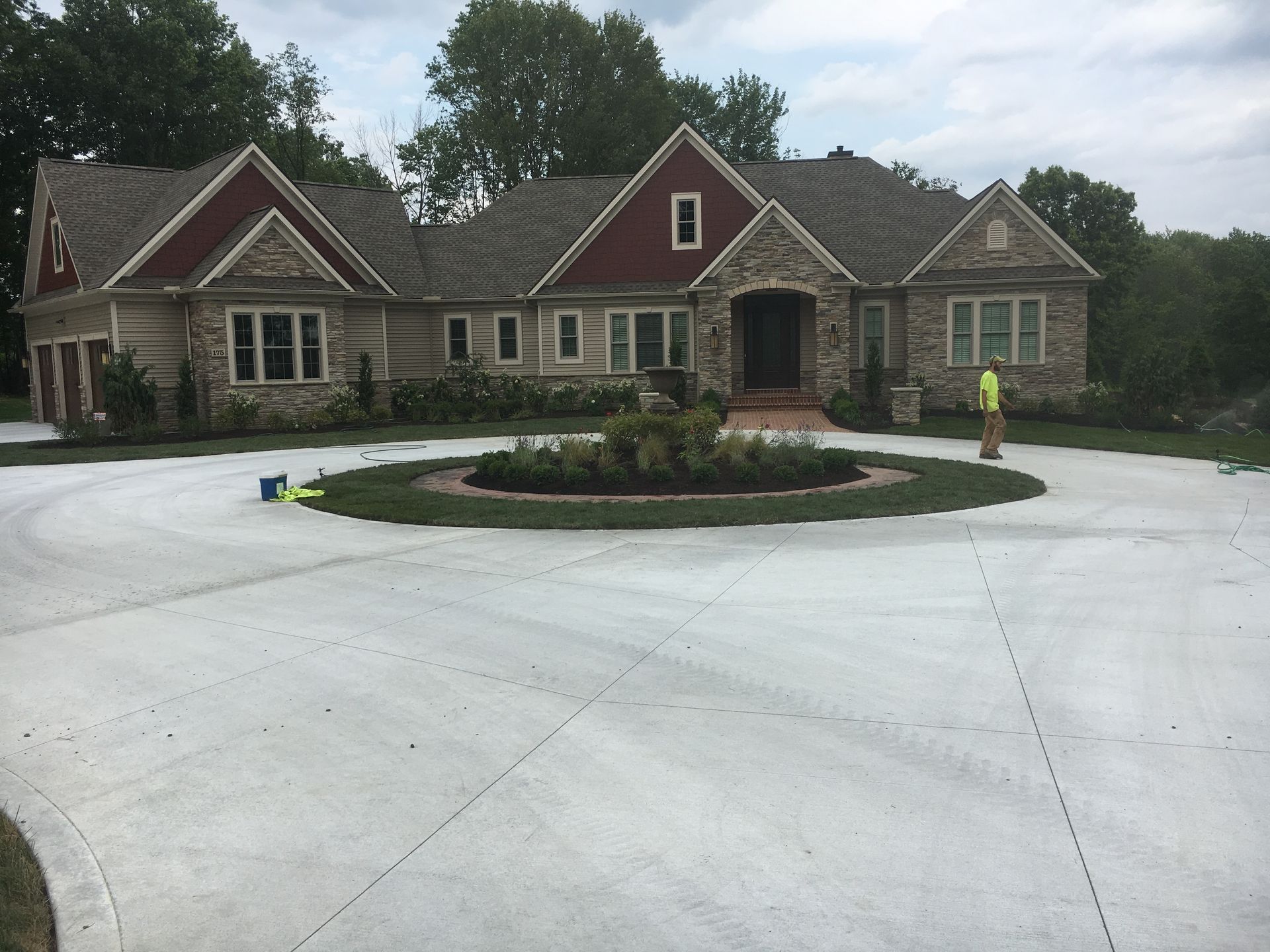 Large stone house with red roofs and a circular driveway, surrounded by trees and landscaping.