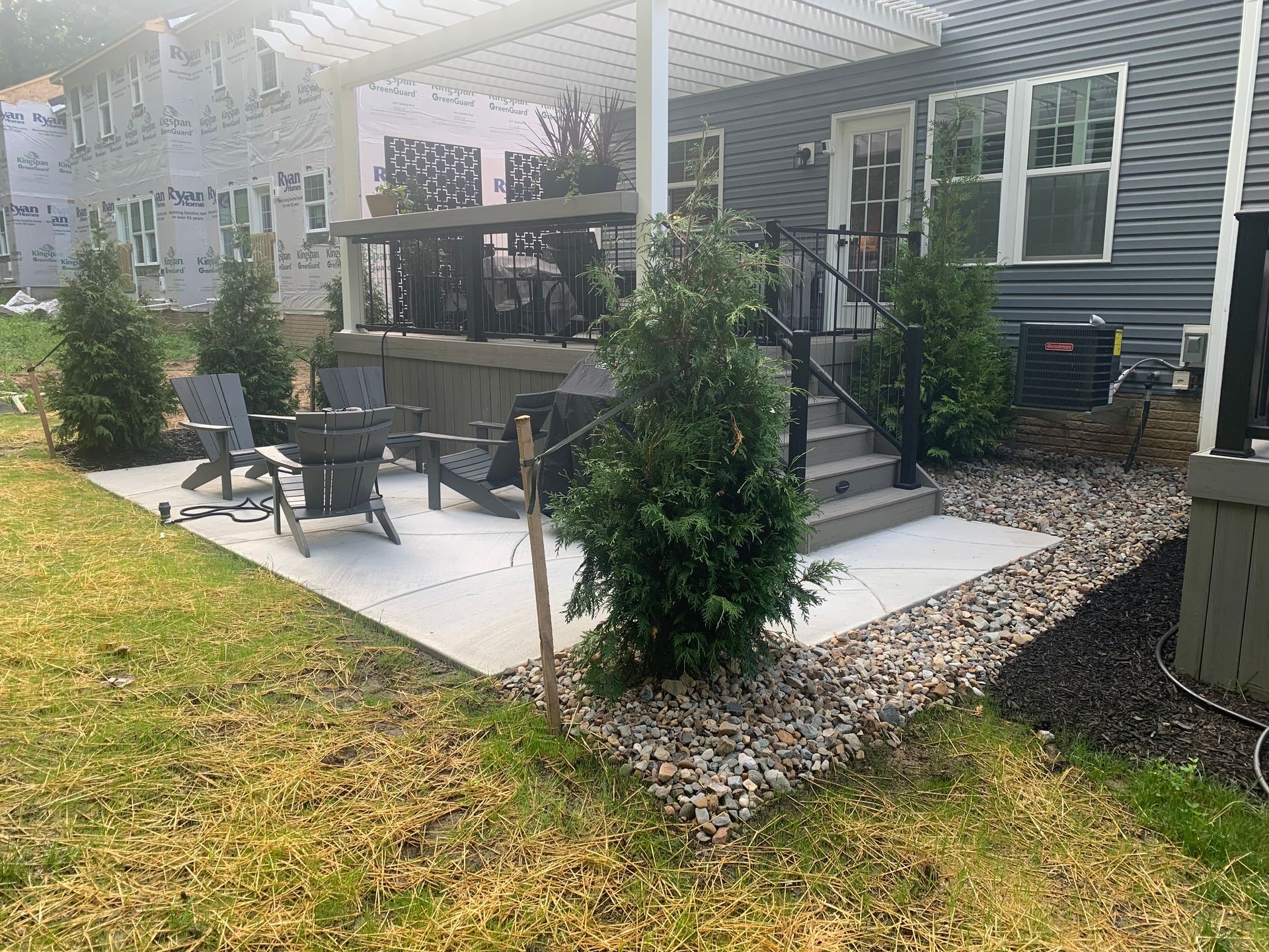 Covered patio with black outdoor dining set and white pergola beside a house and lawn