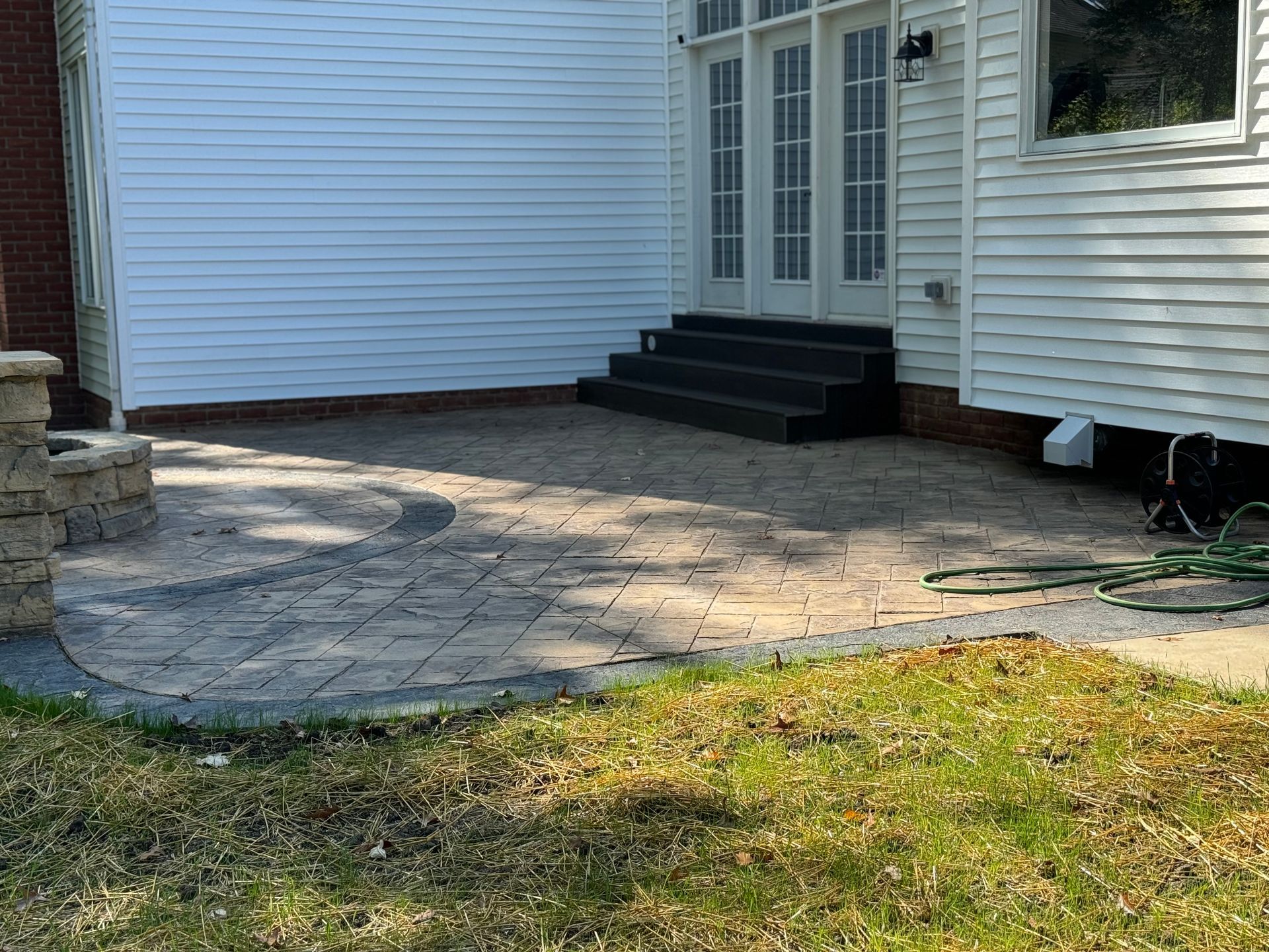 Stone patio leading to black steps and white French doors beside a house with siding and lawn.