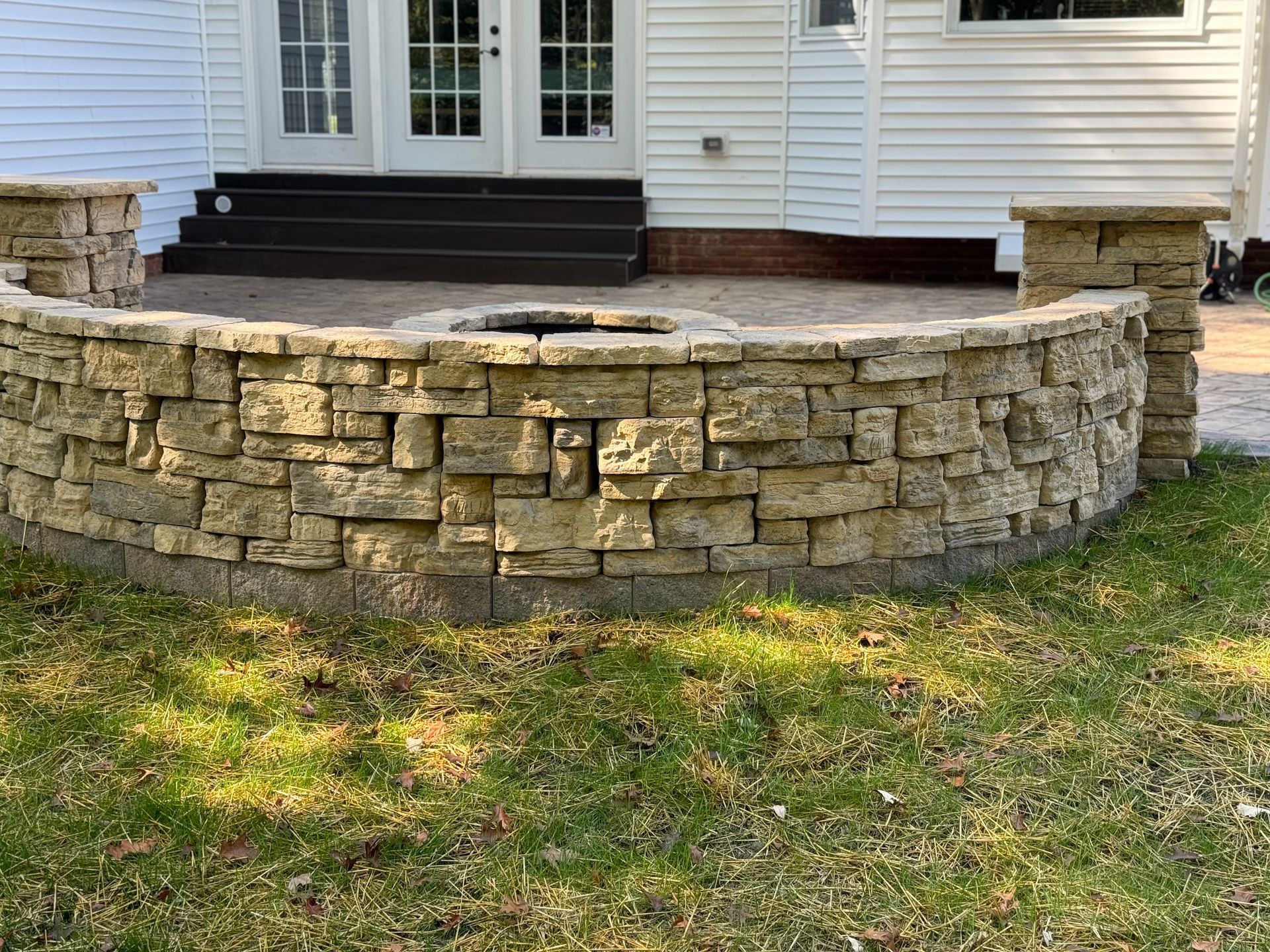 Stone retaining wall with decorative block details in front of a white house porch and black steps