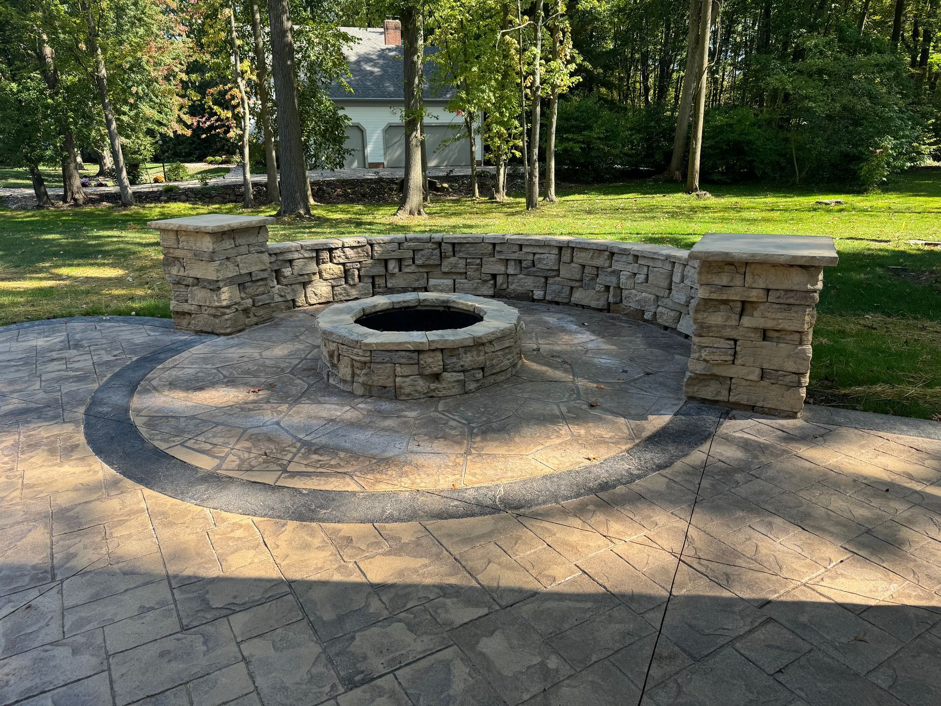 Stone fire pit with curved seating wall on a paved patio in a wooded park area