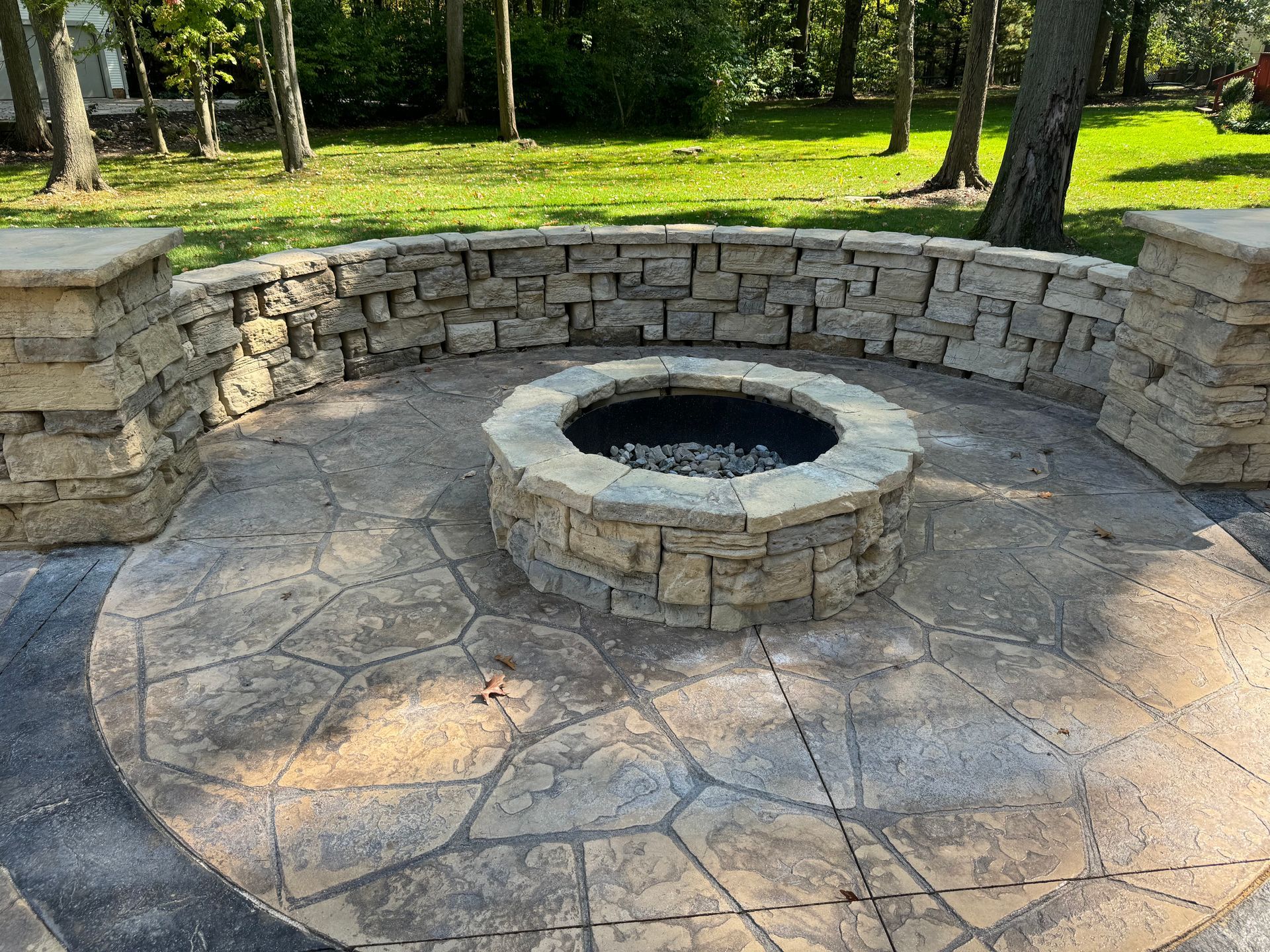 Stone fire pit with circular patio and low curved wall in a park setting