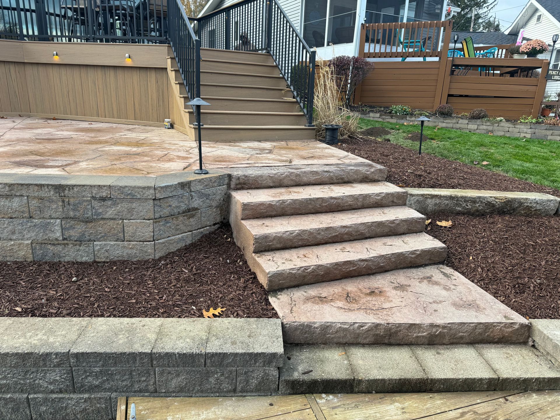 Concrete steps leading to a raised deck with retaining walls and landscaped mulch in a backyard.