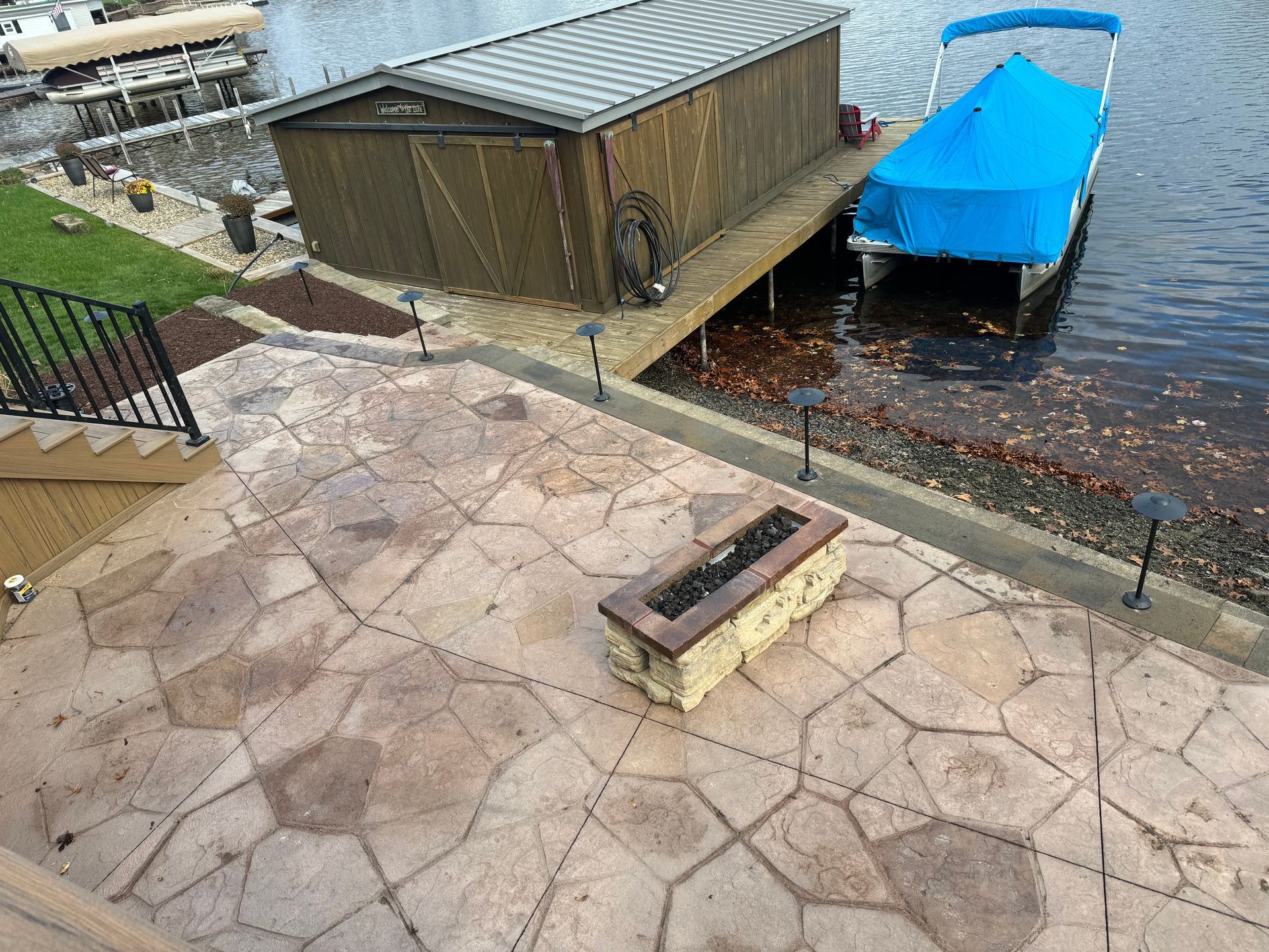 Patio overlooking a lakeside dock with a shed and blue-covered boat, stone fire pit in the foreground