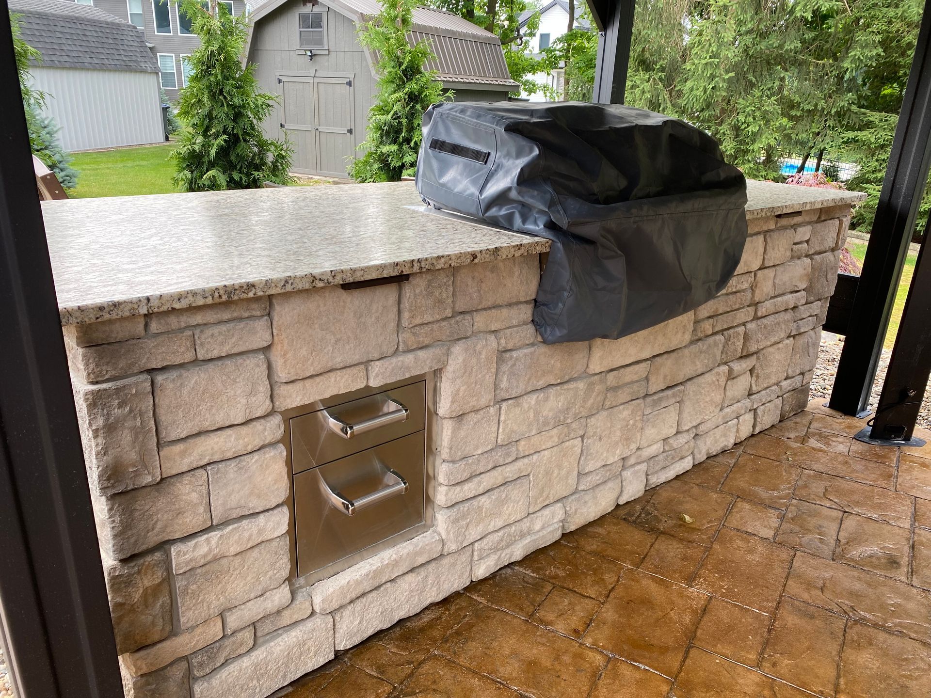 Stone outdoor kitchen with a covered grill on a wet patio