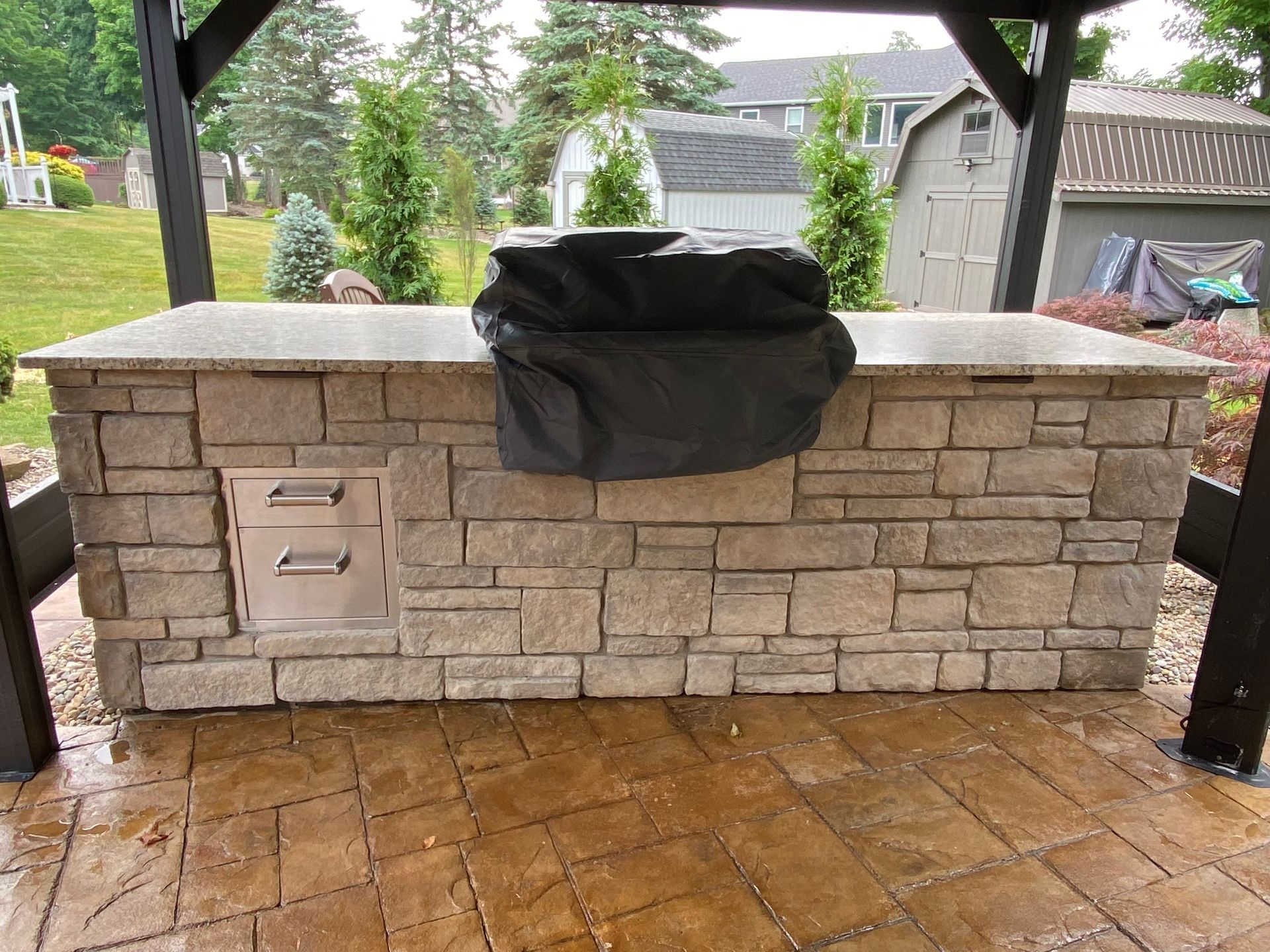Outdoor stone grill island under a patio roof with a covered grill and wet brick floor