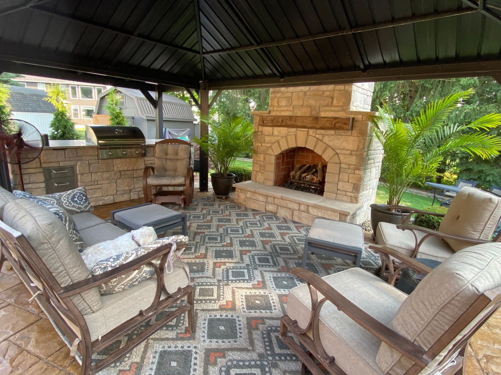 Covered patio with stone fireplace, cushioned seating, and patterned rug.