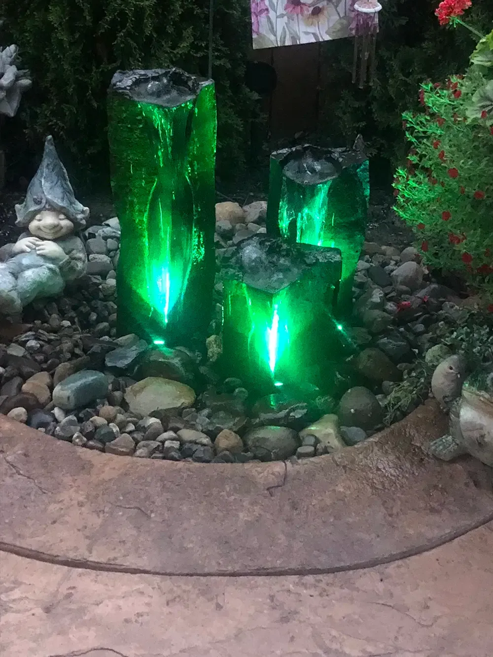 Three glowing green glass garden lights among rocks and plants in a landscaped bed.