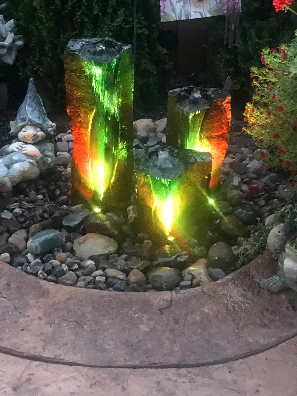 Colorful illuminated garden water features with green, red, and yellow lights among rocks in a landscaped bed.