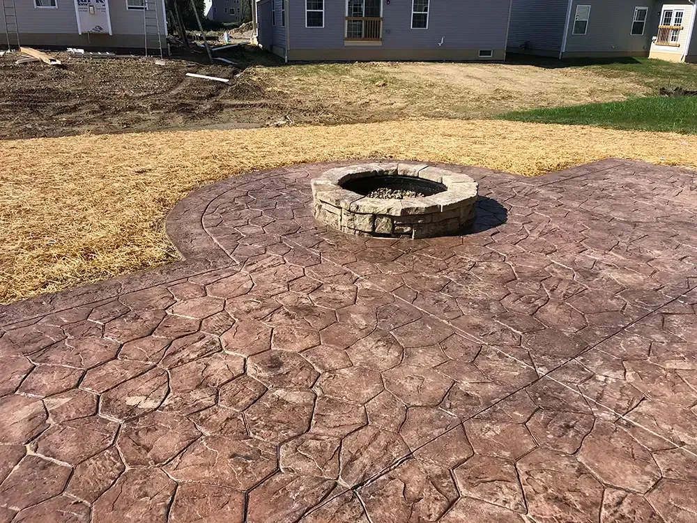 Stamped concrete patio with a circular stone fire pit in a backyard.
