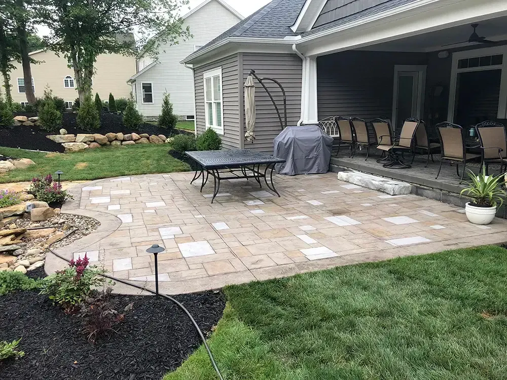 Patio with outdoor furniture, stone pavers, grill, and landscaped garden beside a house.