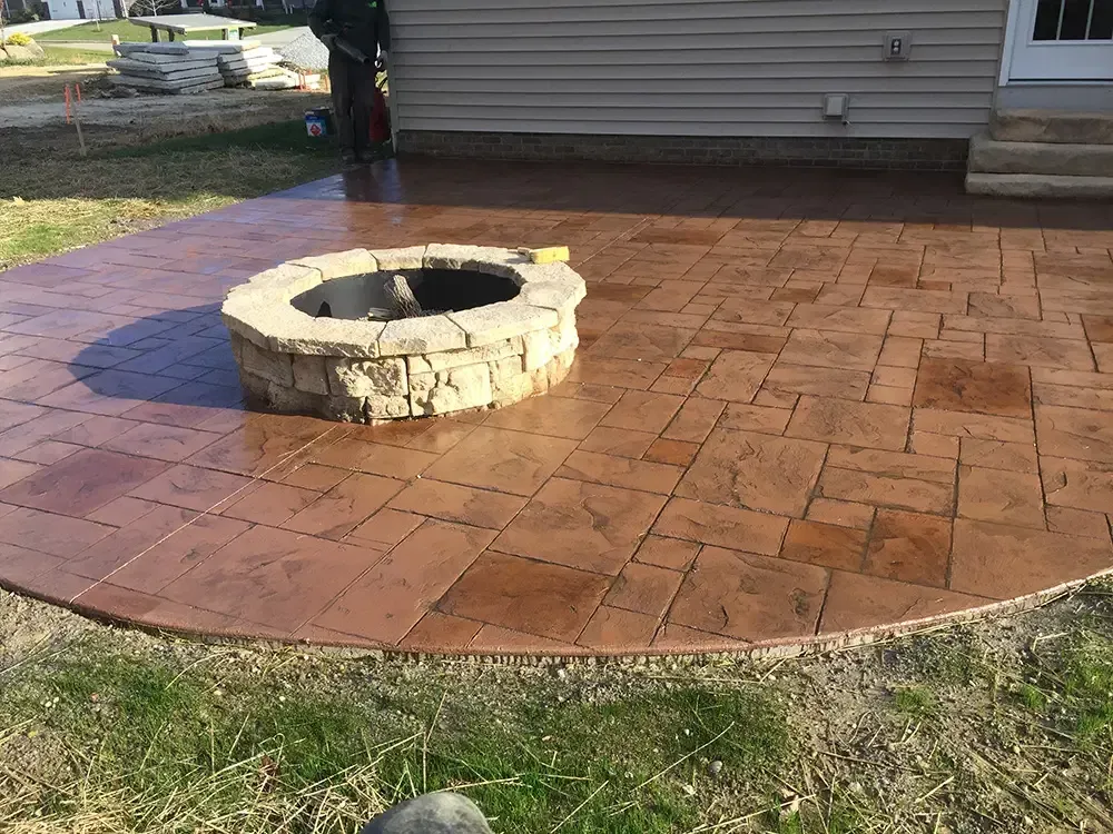 Stamped concrete patio with a stone fire pit beside a house.