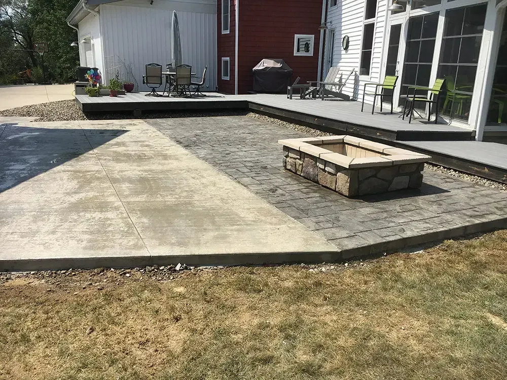 Backyard patio with concrete and paver sections, stone fire pit, and a house with a deck and sliding doors.